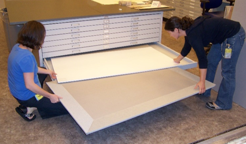 Two people place an oversized print on a rigid support board