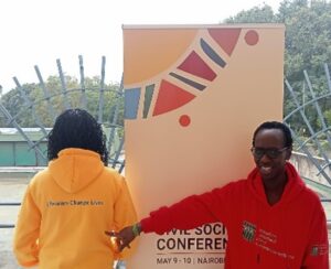 IFLA participants standing in front of a roll-up banner with Civil Society Conference. Woman on the left with mid-length hair, and a yellow hoodie with Libraries Change Lives in green letters. Woman on the right facing us, with short hair and glasses, and a hoodie with the IFLA logo